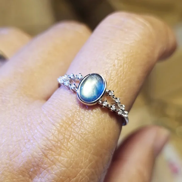 DR-SIL-03-07 Silberring mit ovalem, blau schimmerndem Mondstein und funkelnden Zirkonia-Verzierungen, am Finger getragen.