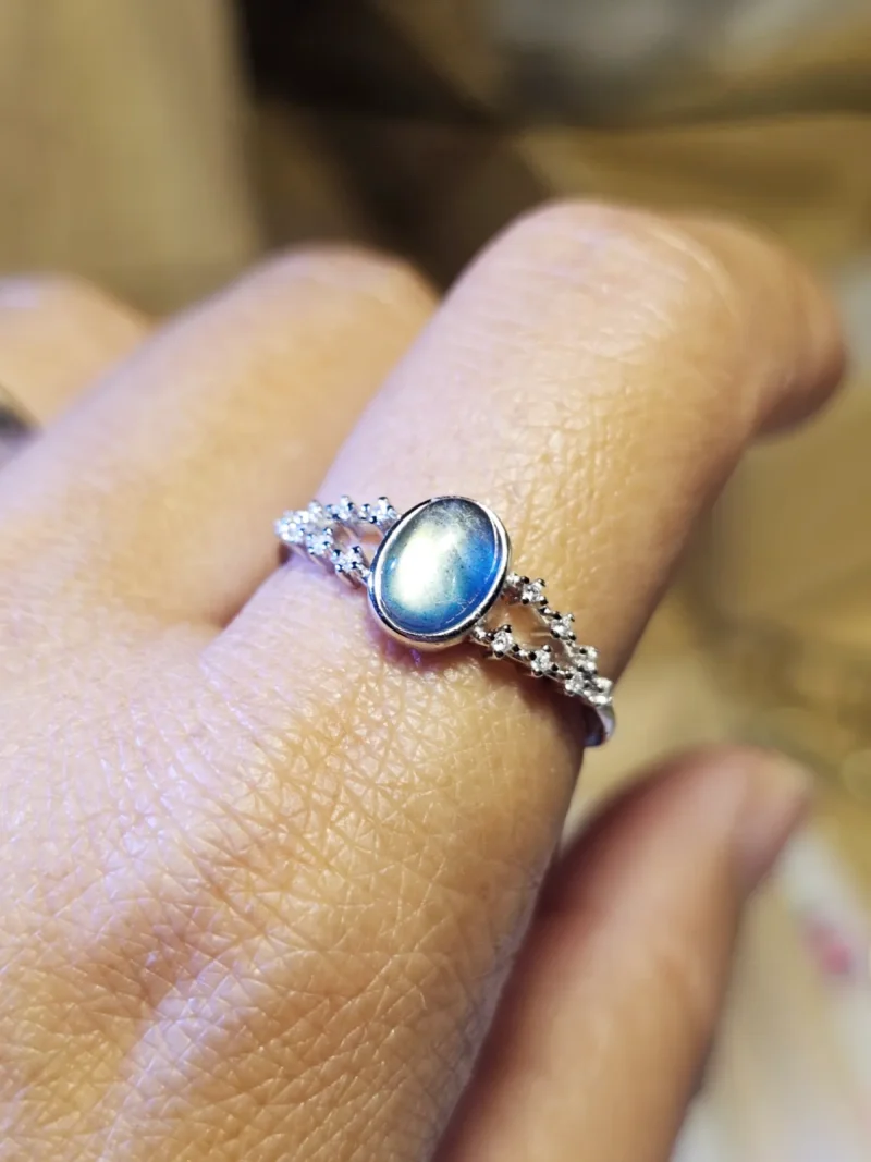 DR-SIL-03-07 Silberring mit ovalem, blau schimmerndem Mondstein und funkelnden Zirkonia-Verzierungen, am Finger getragen.