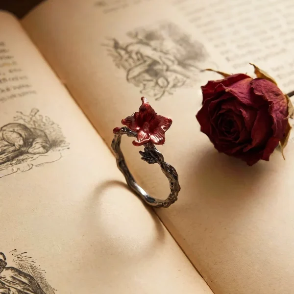 DR-GTC-01-5 Gotischer Lilienring mit roter Blüte und silberfarbener Vintage-Ringschiene im Dark Romantic Stil, auf einer offenen Buch.