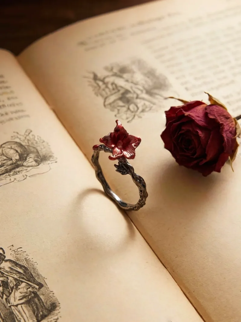 DR-GTC-01-5 Gotischer Lilienring mit roter Blüte und silberfarbener Vintage-Ringschiene im Dark Romantic Stil, auf einer offenen Buch.