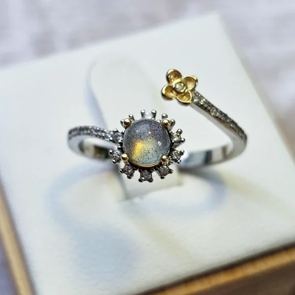 DR-SIL-04-01 Offener Silberring mit rundem, schimmerndem Mondstein, funkelnden Zirkonia und goldfarbenem Blumen-Detail.
