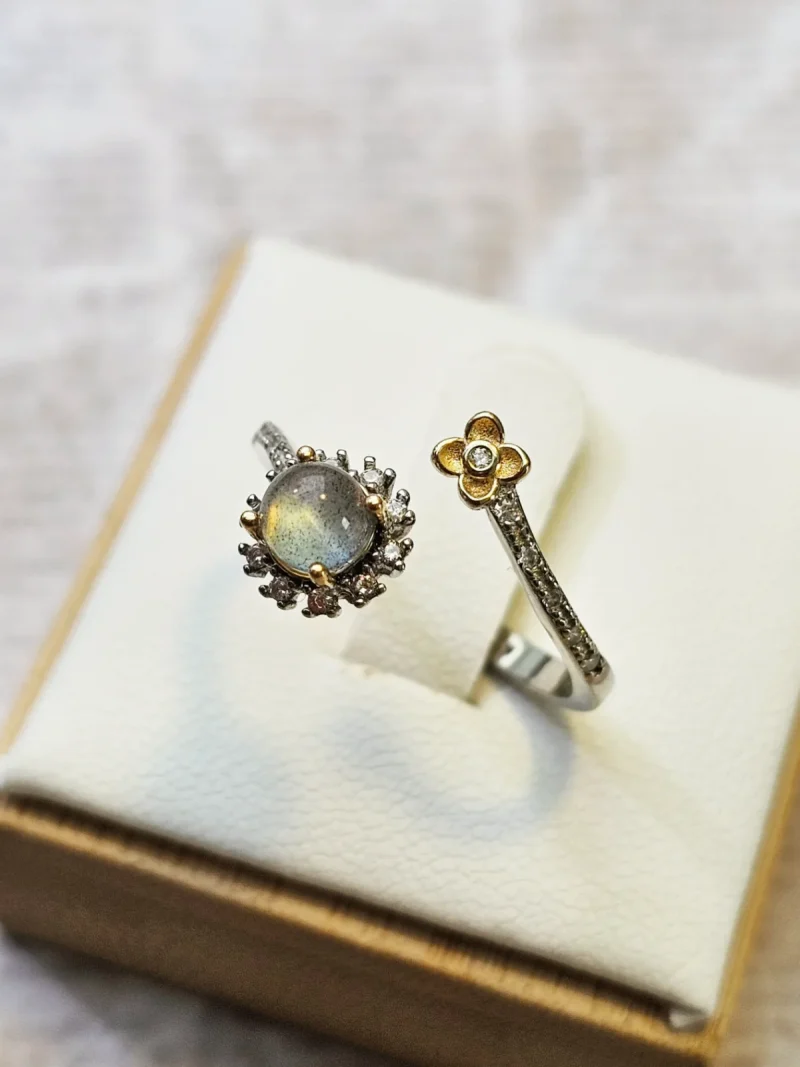 DR-SIL-04-2 Offener Silberring mit rundem, schimmerndem Mondstein, funkelnden Zirkonia und goldfarbenem Blumen-Detail.