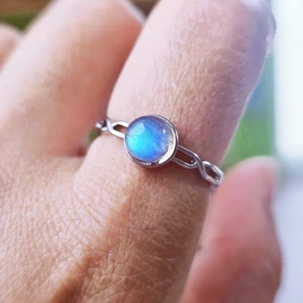 DR-TDS-09-05 Filigraner Silberring mit rundem, intensiv blau schimmerndem Mondstein, am Finger getragen.
