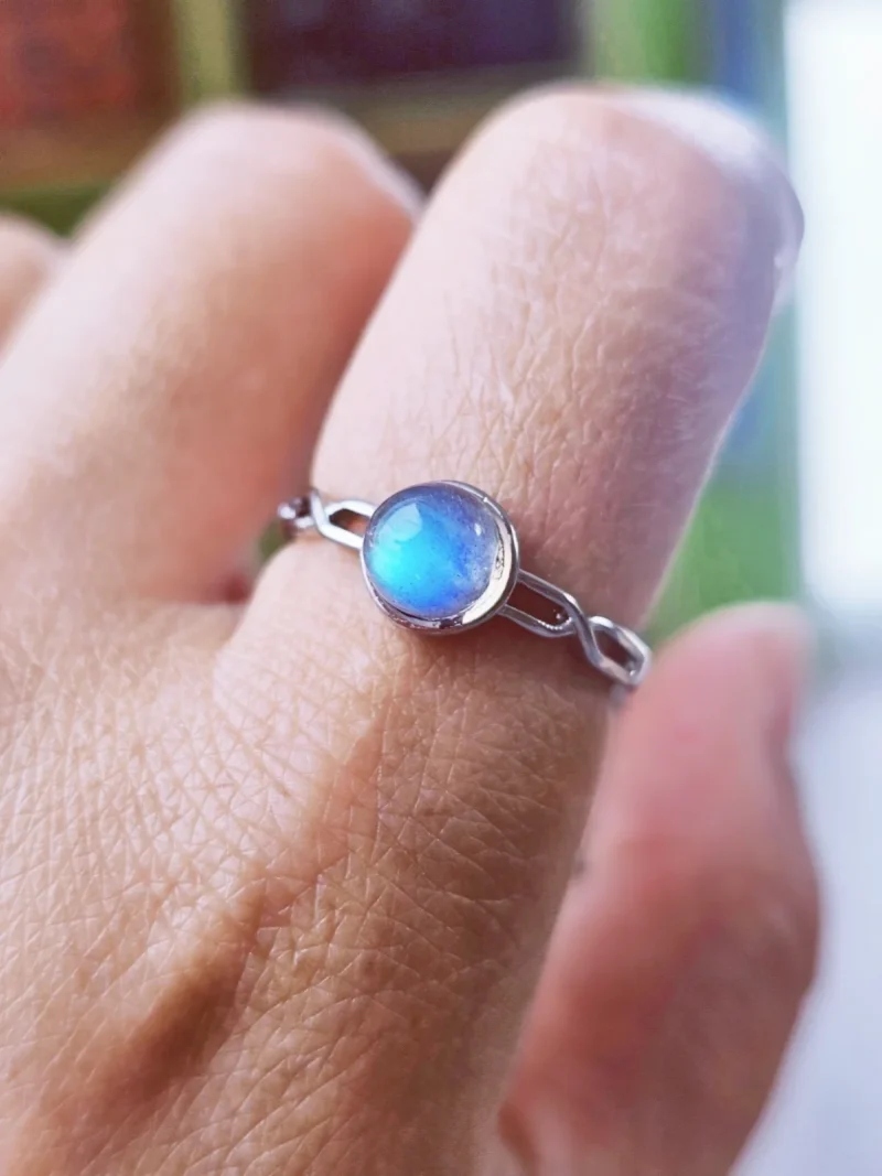 DR-TDS-09-05 Filigraner Silberring mit rundem, intensiv blau schimmerndem Mondstein, am Finger getragen.