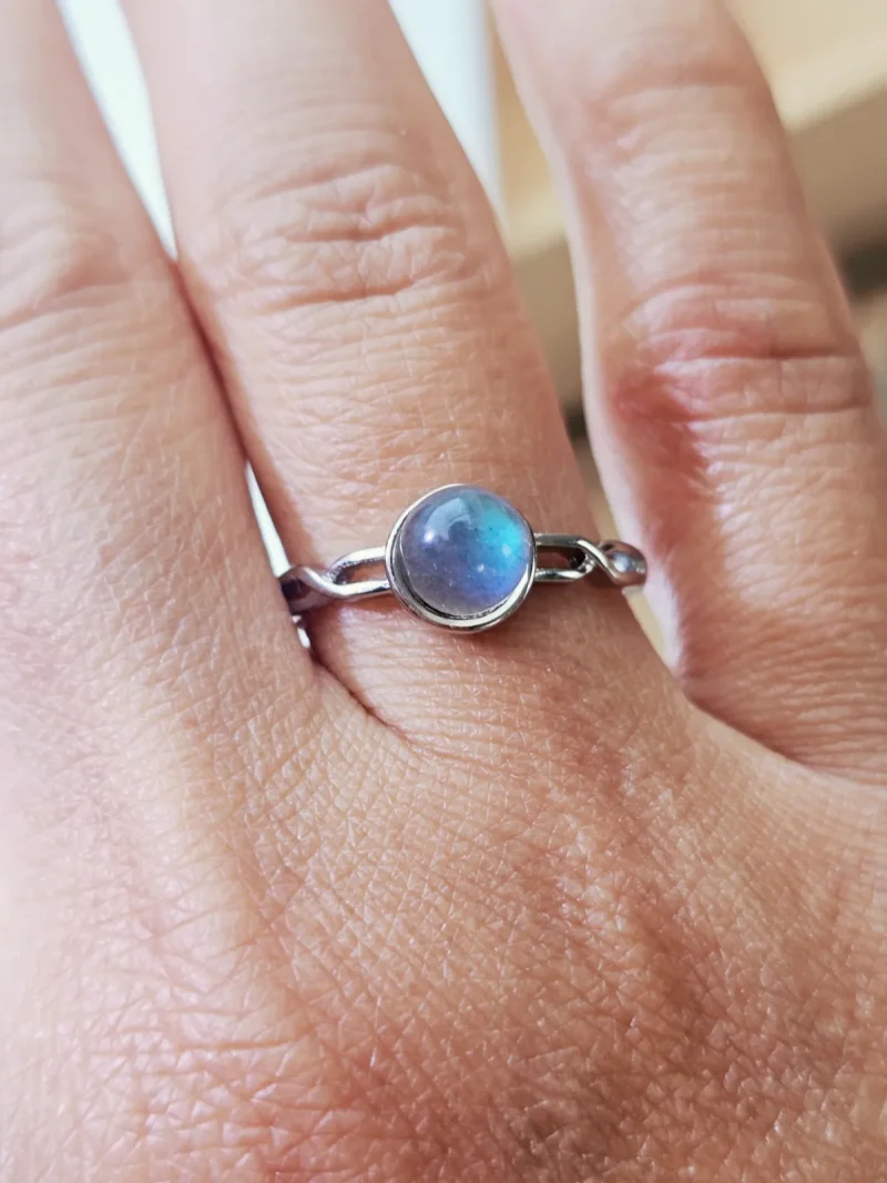 DR-TDS-09-06 Filigraner Silberring mit rundem, intensiv blau schimmerndem Mondstein, am Finger getragen.